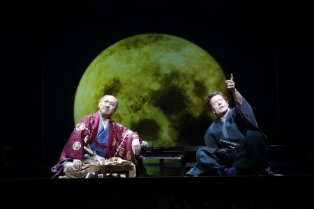 2 men sat on a theatre stage performing in front of an image of the moon