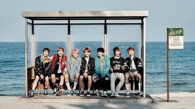 A Korean boy band standing in a bus stop with the sea in the background