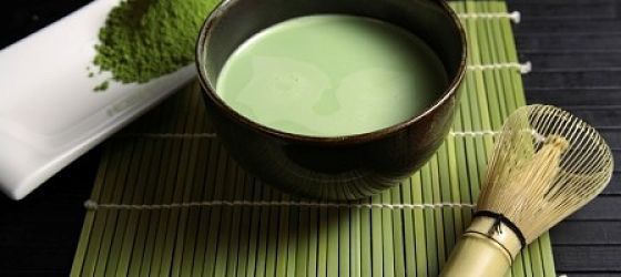 Some green tea in a bowl on a table with some tea powder