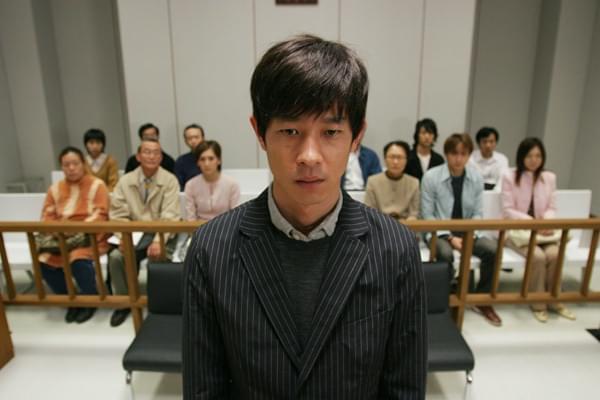 A Japanese man in a courtroom with people sat behind him