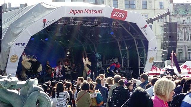 A crowd watching a Japanese pop group on an outdoor stage