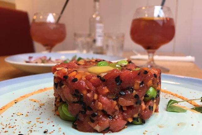 A plate of Steak tartare, edamame, black sesame and quail egg with some cocktails on a table