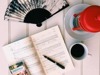 A diary, a fan, a pen and a cup of coffee on a desk