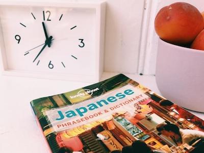 A Japanese book, a clock and a bowl of peaches on a table